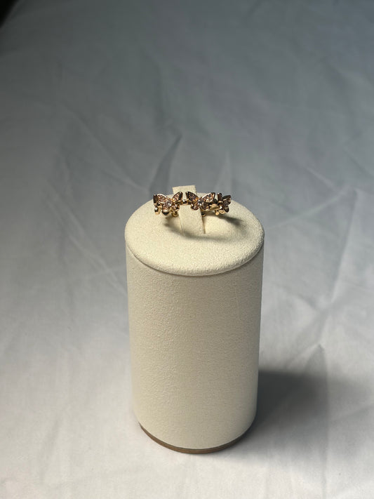 A delicate gold ring with small clear stones, displayed on a textured cream-colored cylindrical stand against a light gray fabric background.