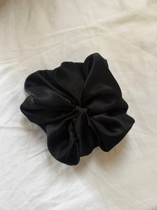 A black silk hair scrunchie resting on a white fabric background.