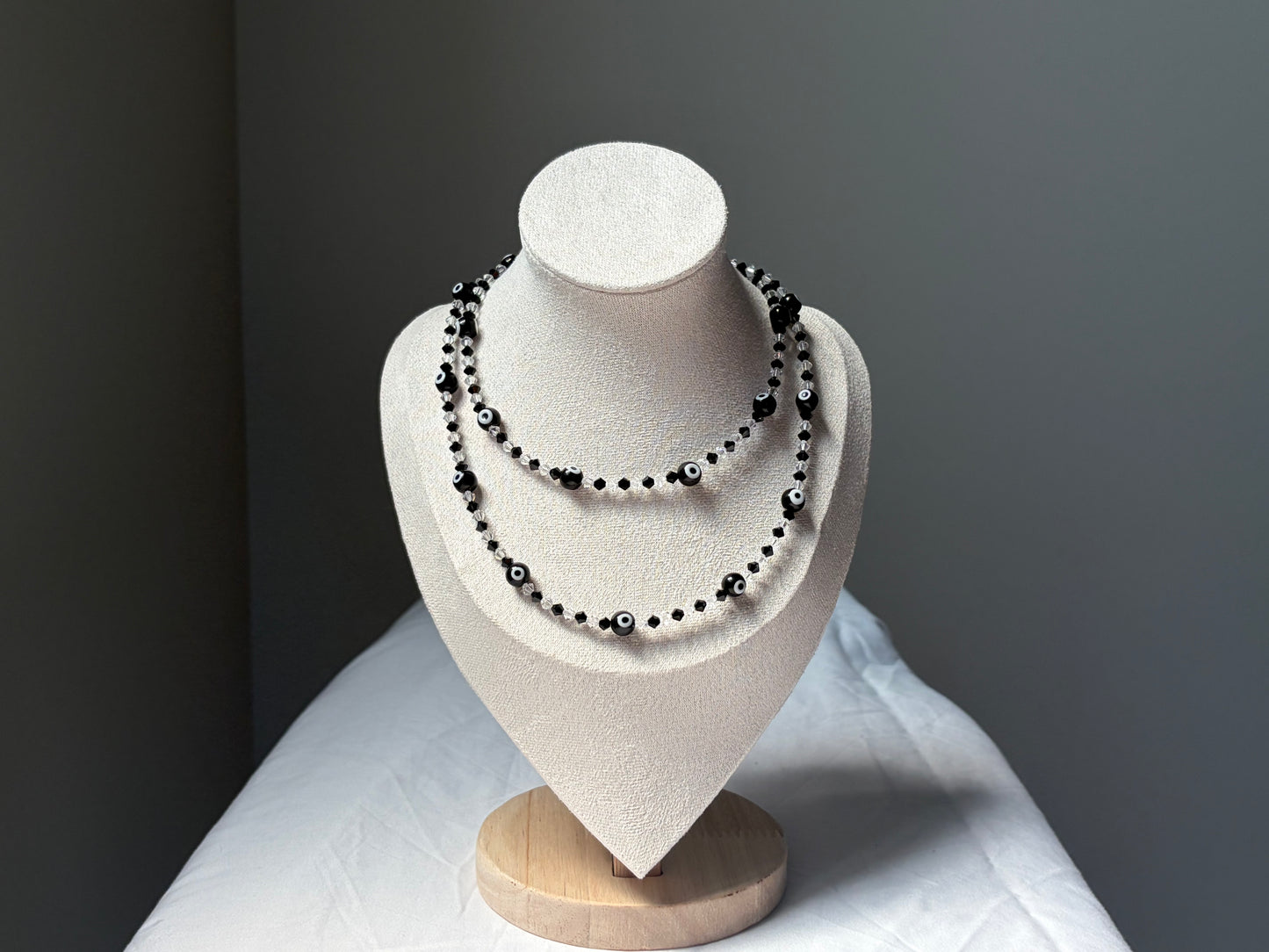 A double-strand Swarovski crystal beaded necklace with black and white beads displayed on a cream-colored jewelry bust against a dark gray background.