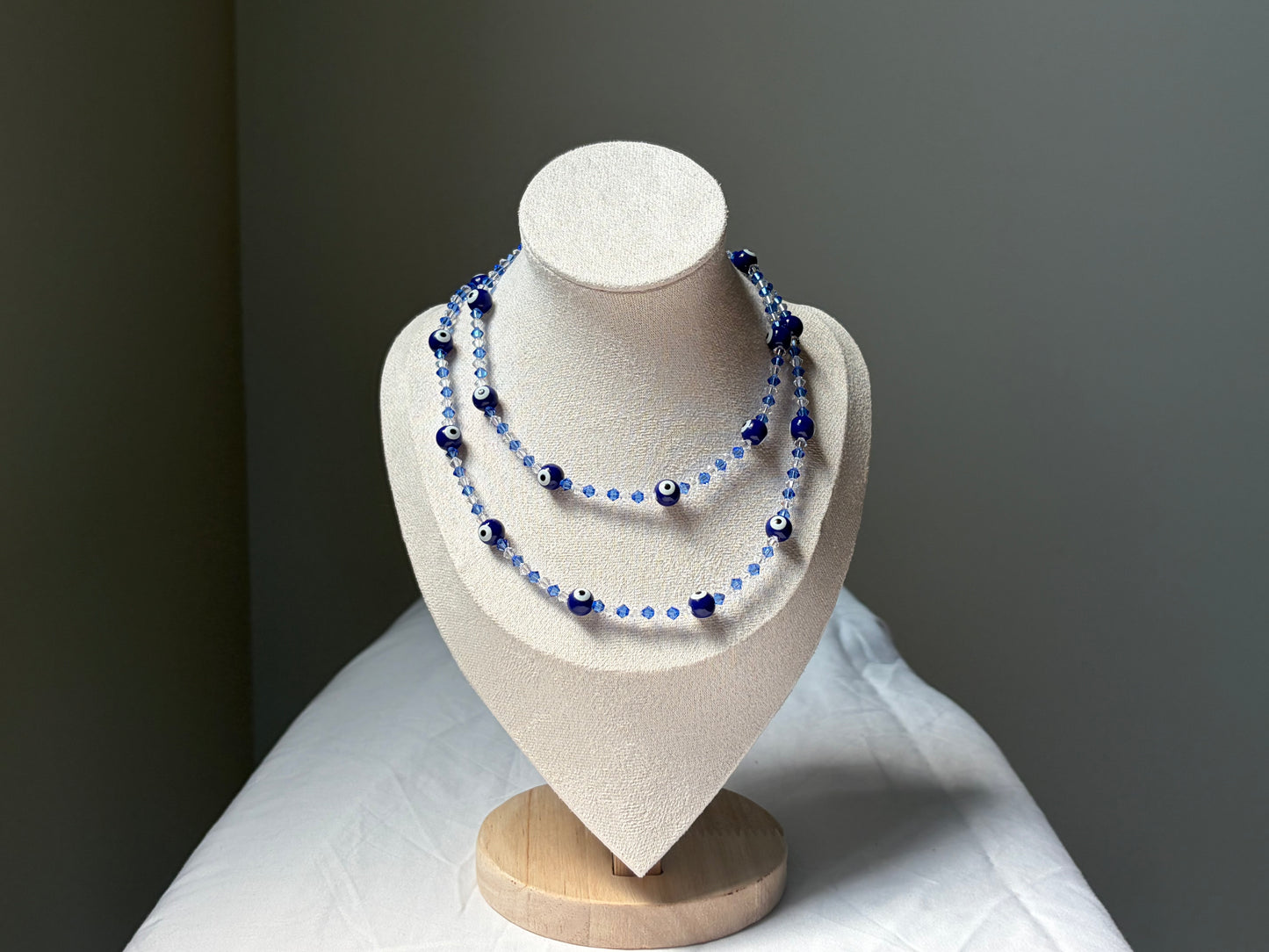A double-strand Swarovski cryatl beaded necklace with dark blue and light blue beads, displayed on a cream-colored jewelry bust against a dark gray background.