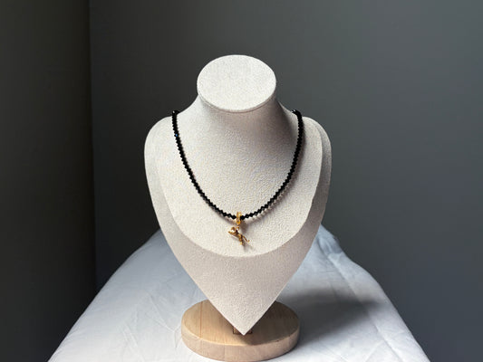 A black Swarovski crystal beaded necklace with a small gold-toned leopard charm pendant displayed on a white jewelry bust against a dark gray background.