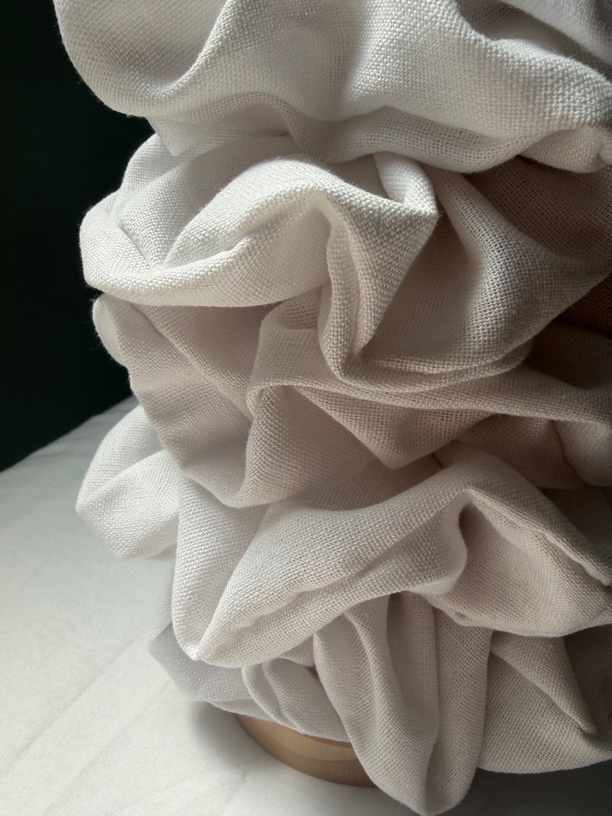 A close-up of a linen scrunchies, gathered into a ruffled bouquet shape on a wooden stand.