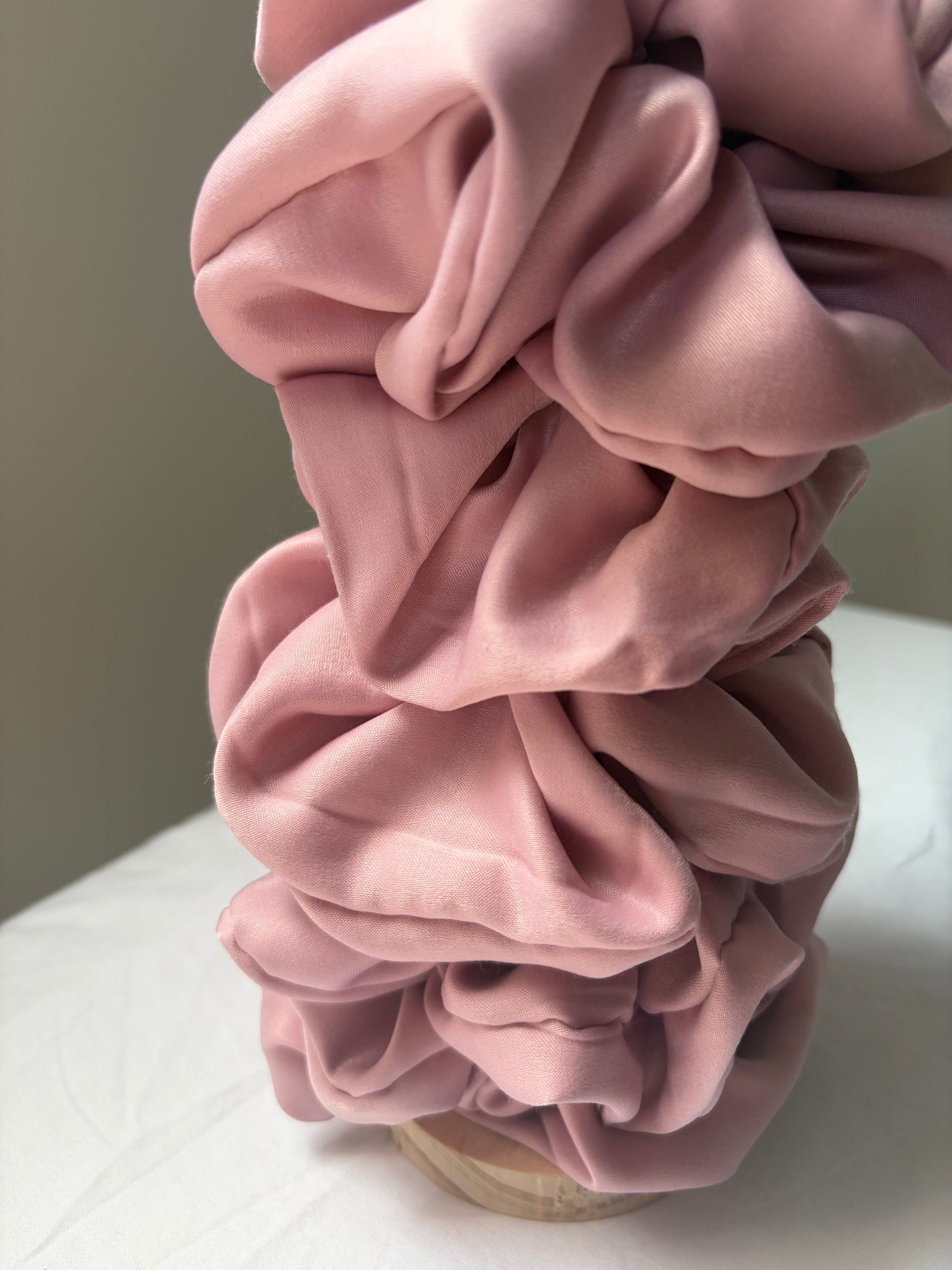 A dusty pink satin hair scrunchie styled in a stacked, layered arrangement on a light-colored surface.