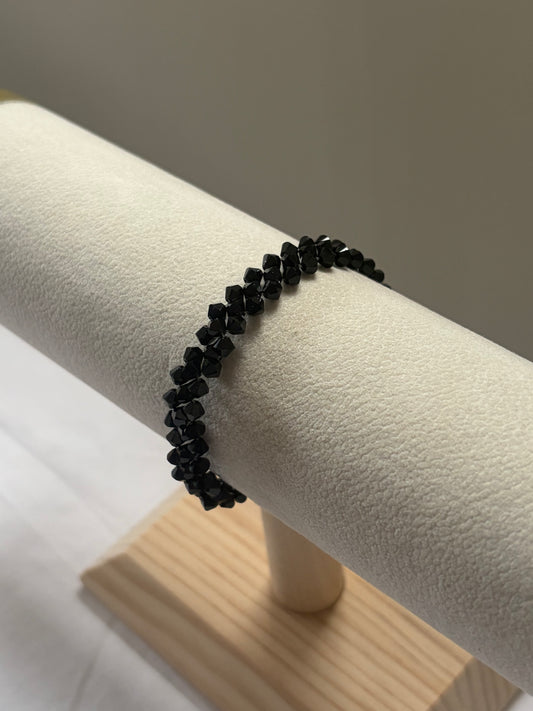 A black Swarovski crystal beaded stretch bracelet displayed on a cream-colored jewelry display stand.