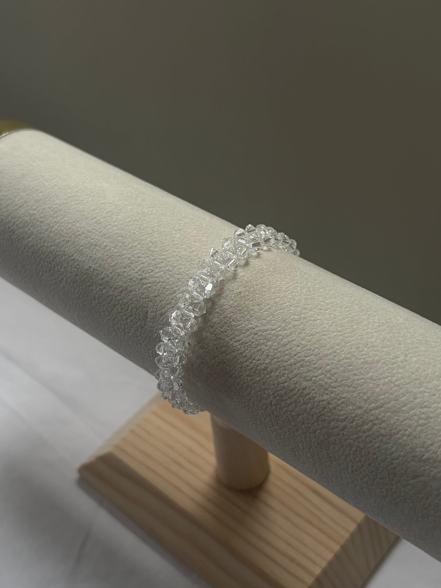 A clear faceted gemstone Swarovski crystal beaded bracelet displayed on a cream-colored jewelry display stand.
