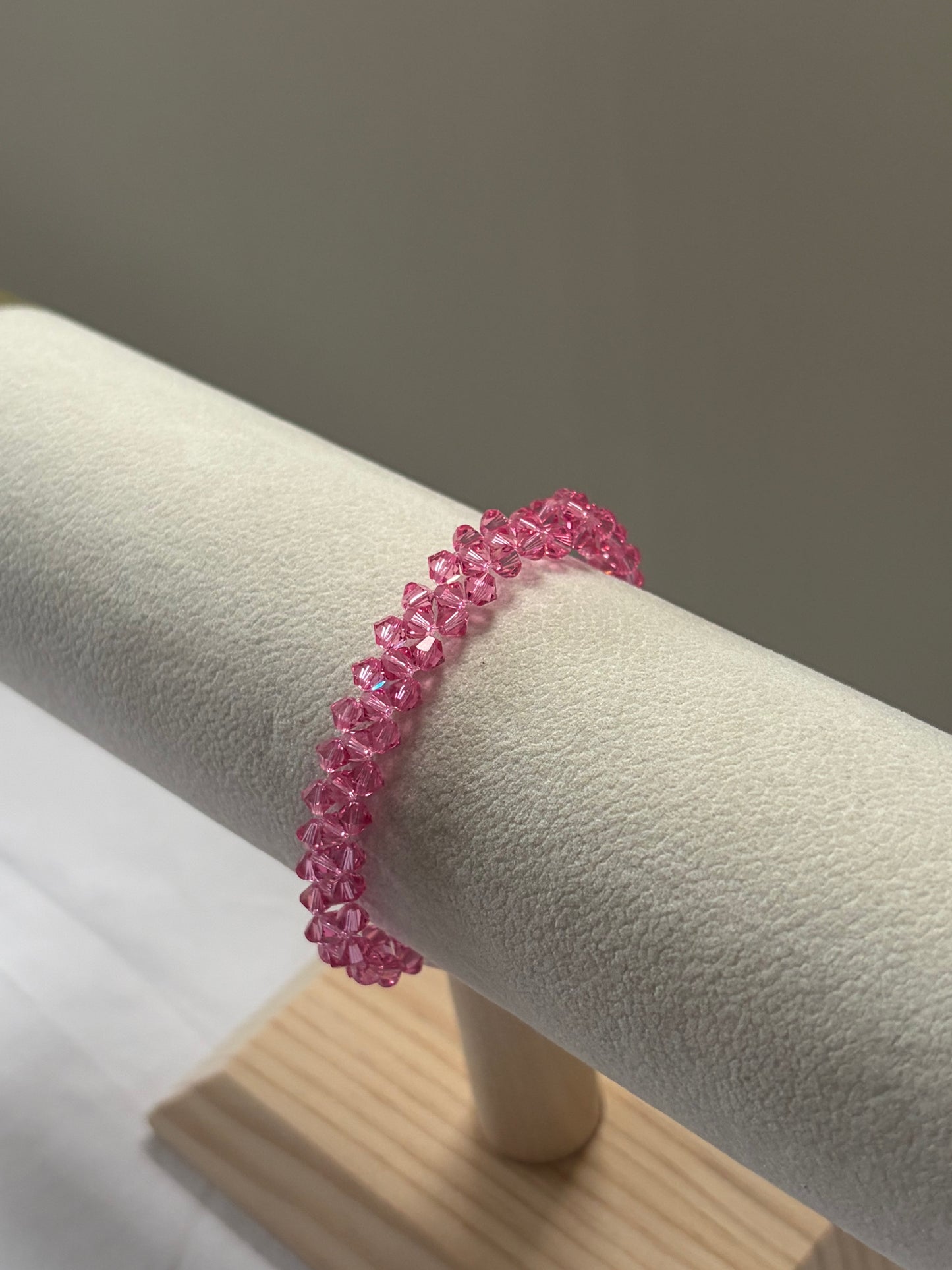 A pink Swarovski crystal beaded bracelet displayed on a cream-colored jewelry stand against a neutral gray background.