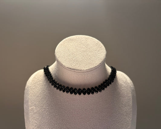 A black Swarovski crystal beaded solid choker necklace displayed on a white textured jewelry bust against a neutral gray background.