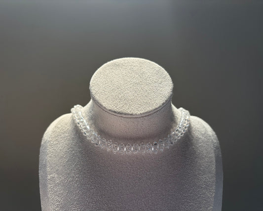A clear Swarovski crystal beaded solid choker necklace displayed on a textured light gray jewelry bust against a dark gray gradient background.