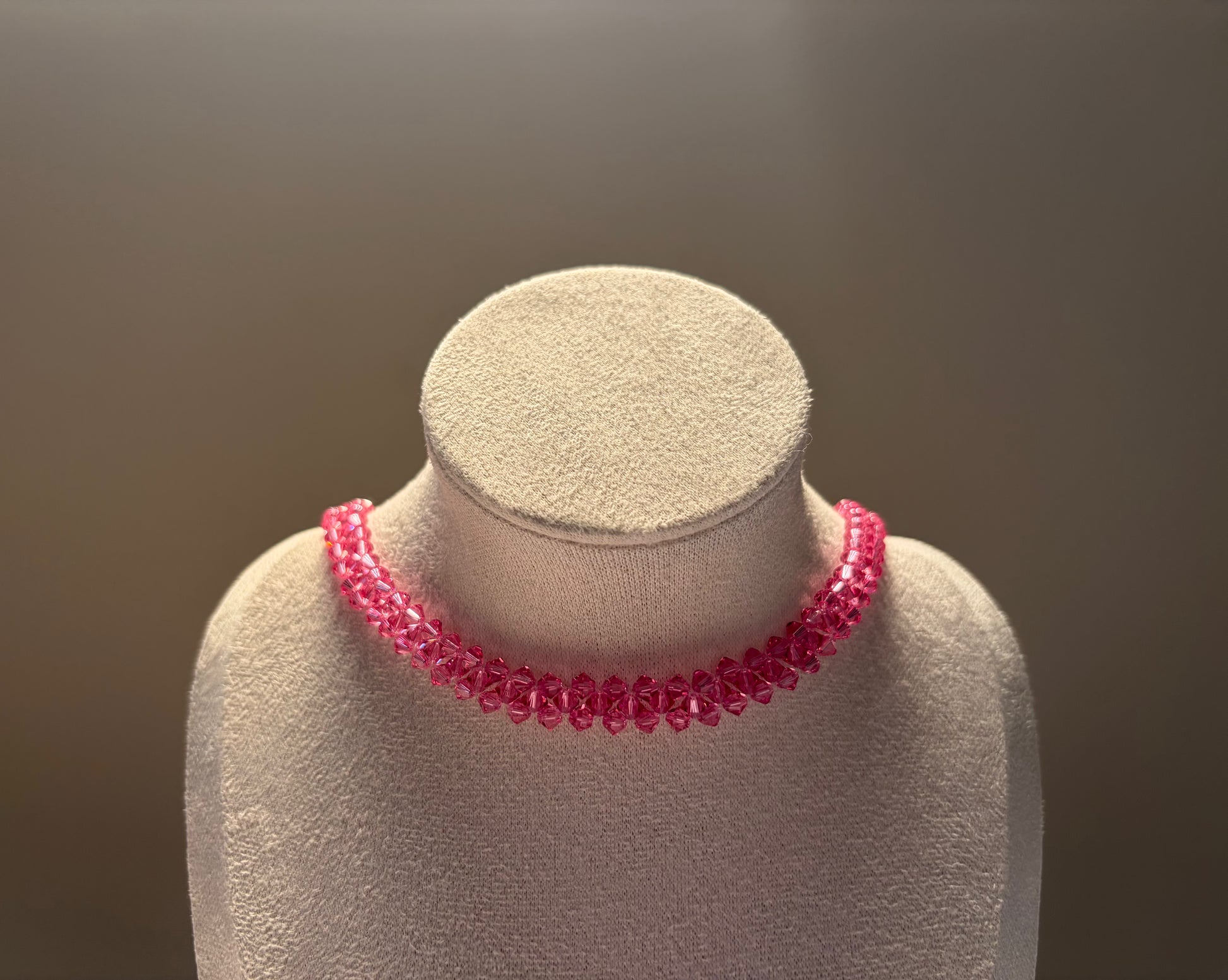 A bright pink Swarovski crystal beaded choker necklace displayed on a textured beige jewelry bust against a soft gray background.