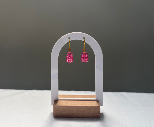 A pair of pink faceted Swarovski crystal beaded dangle earrings with gold-toned hooks, displayed on a white arched stand with a wooden base against a dark gray background.