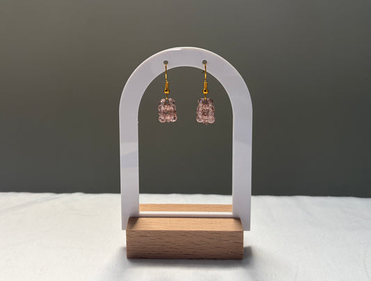 A pair of rose gold Swarovski crystal faceted bead drop earrings with gold hooks, displayed on a white arch stand with a wooden base against a dark gray background.