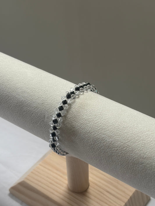 A Swarovski crystal beaded striped bracelet with alternating black and clear faceted beads, displayed on a cream-colored jewelry display stand.