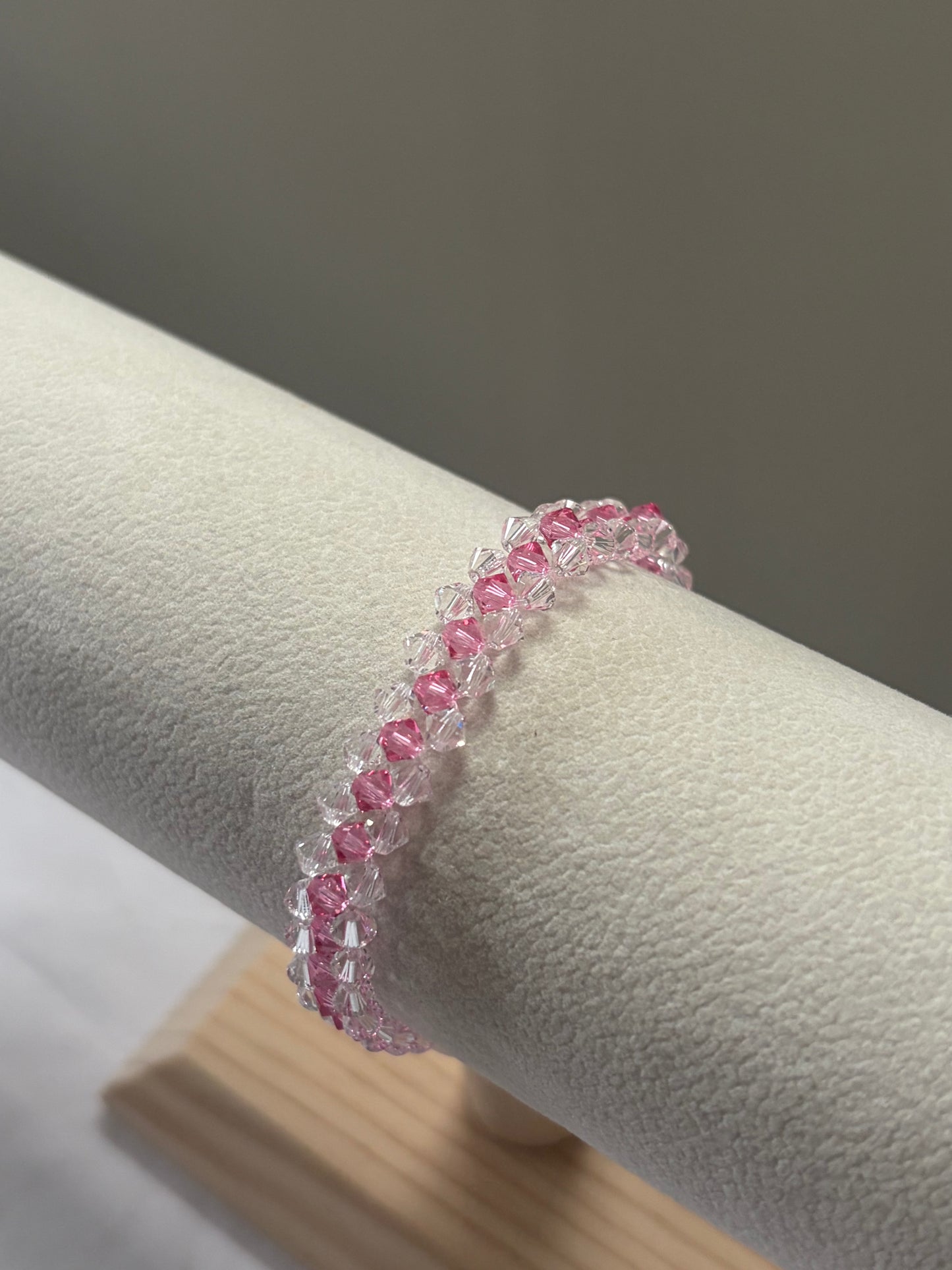 A Swarovski crystal beaded striped bracelet with alternating pink and clear faceted beads, displayed on a cream-colored jewelry stand.