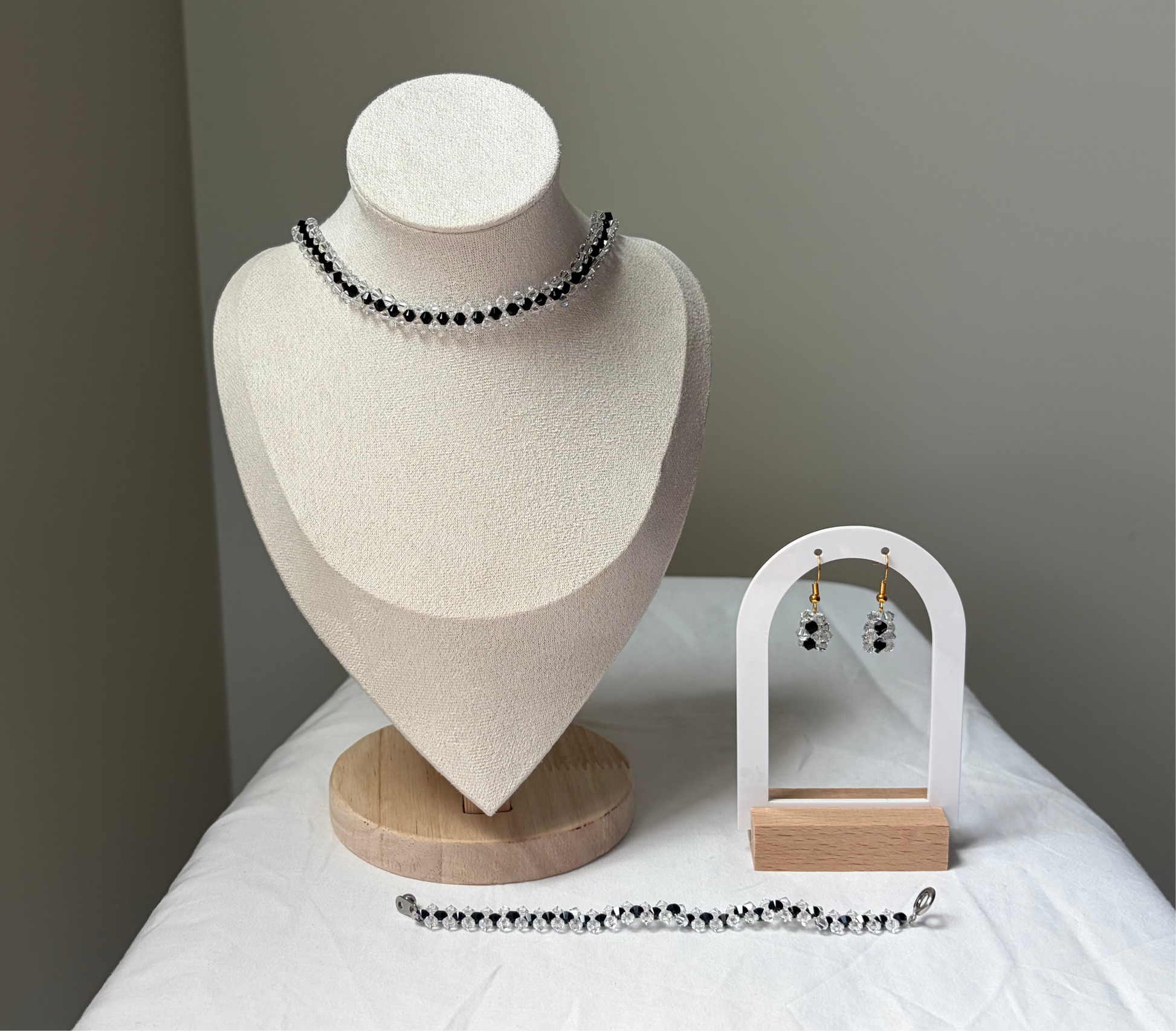 A Swarovski crystal beaded jewelry set displayed on a cream fabric mannequin bust and a small white arch stand, featuring a necklace, bracelet, and matching earrings with black and white striped design. 