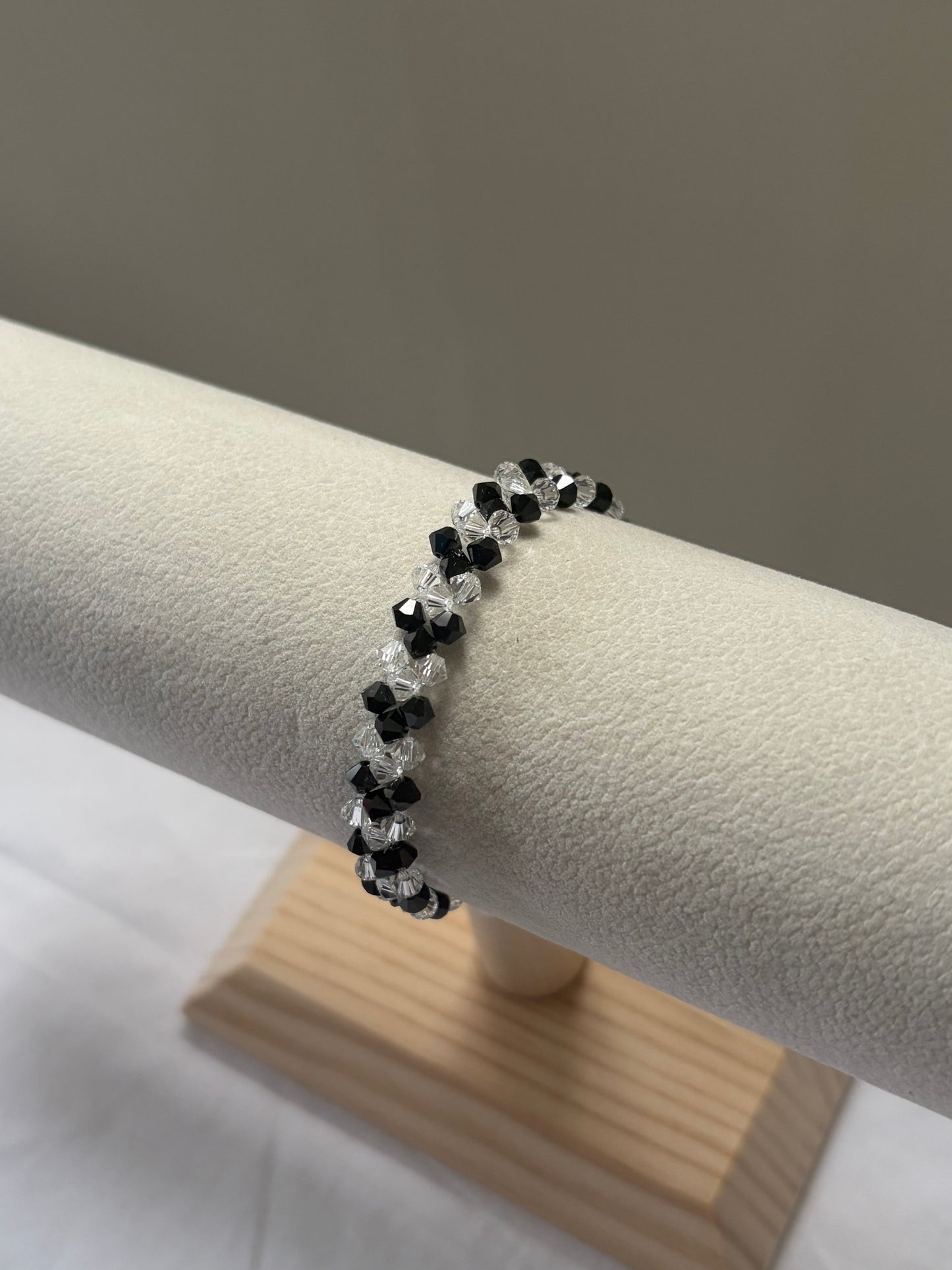 A Swarovski crystal beaded v-bracelet with alternating black and clear faceted beads, displayed on a cream-colored jewelry stand.