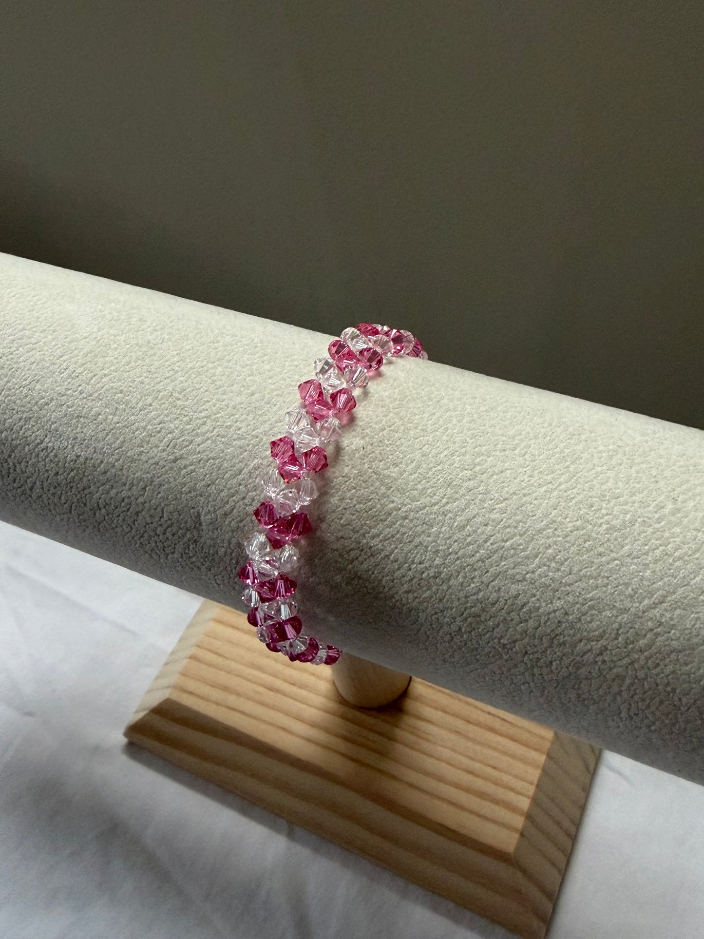 A Swarovski crystal beaded v-bracelet with alternating pink and clear faceted beads, displayed on a textured off-white jewelry stand with a wooden base.