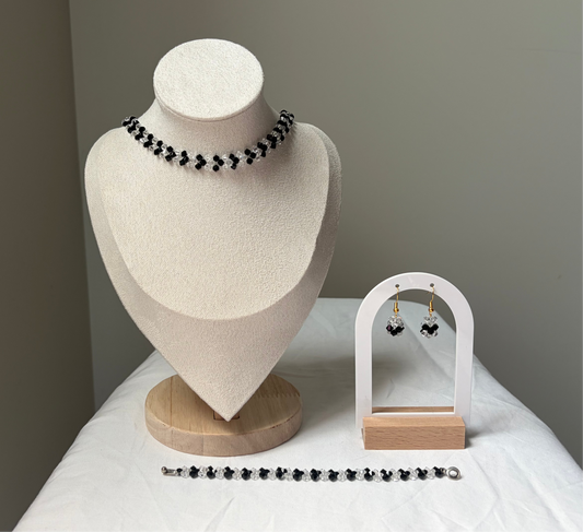 A Swarovski crystal beaded jewelry set displayed on a cream fabric mannequin bust and a small white arch stand, featuring a necklace, bracelet, and matching earrings with black and white v-shaped design. 