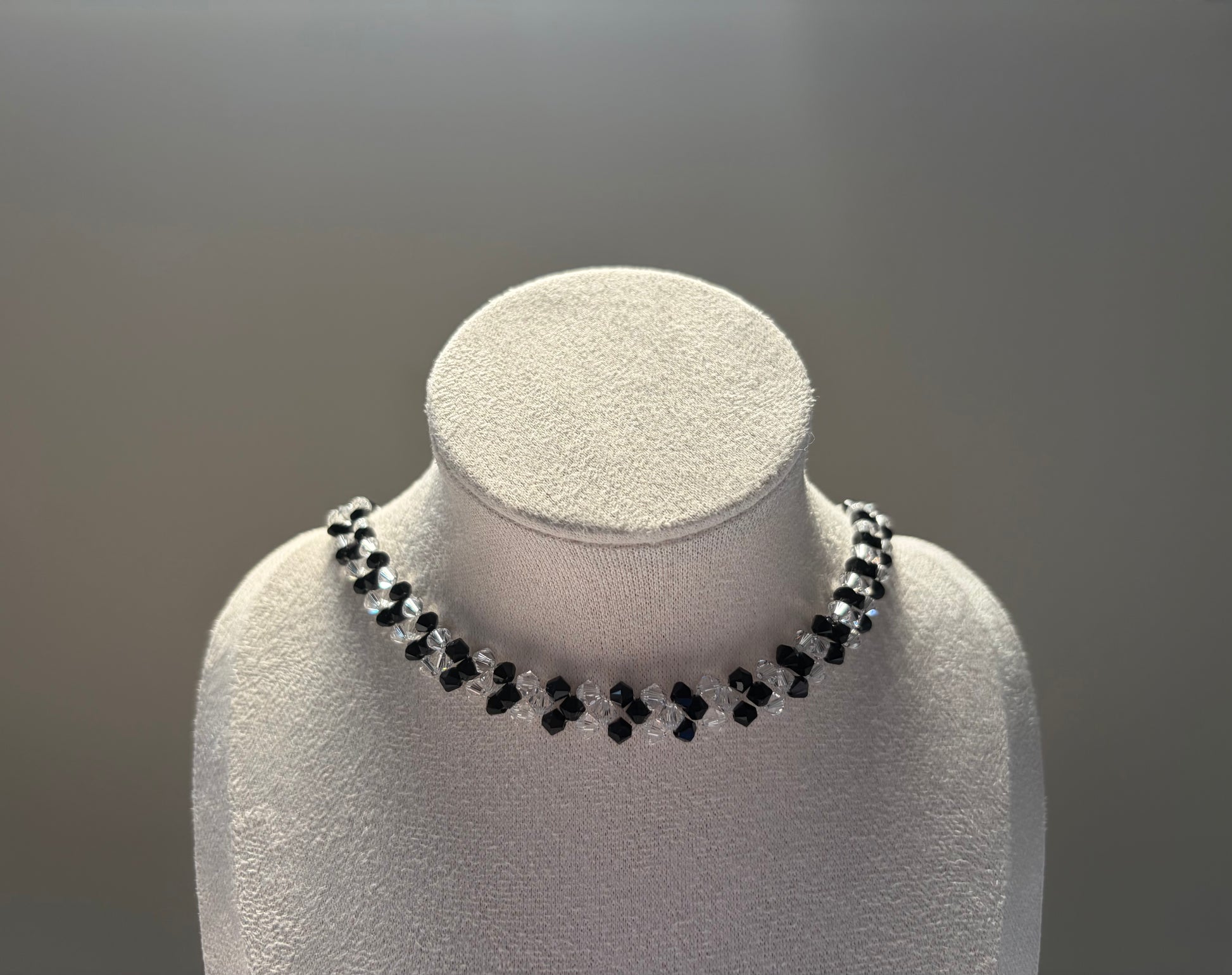 A Swarovski crystal beaded v choker necklace with alternating black and clear beads, displayed on a white textured jewelry bust against a neutral gray background.