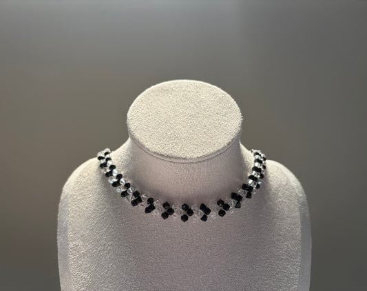 A Swarovski crystal beaded v choker necklace with alternating black and clear beads, displayed on a white textured jewelry bust against a neutral gray background.