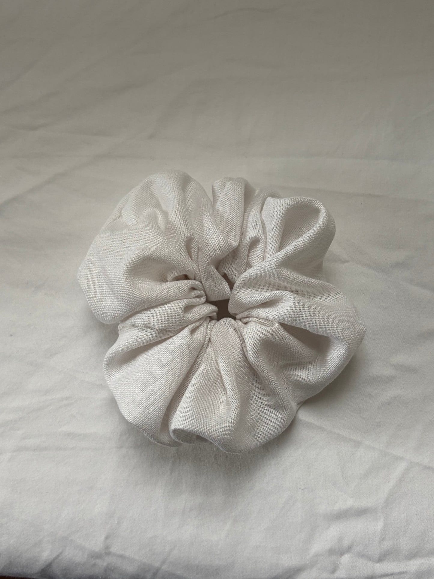 A single white fabric scrunchie made of textured linen material, photographed on white fabric background.