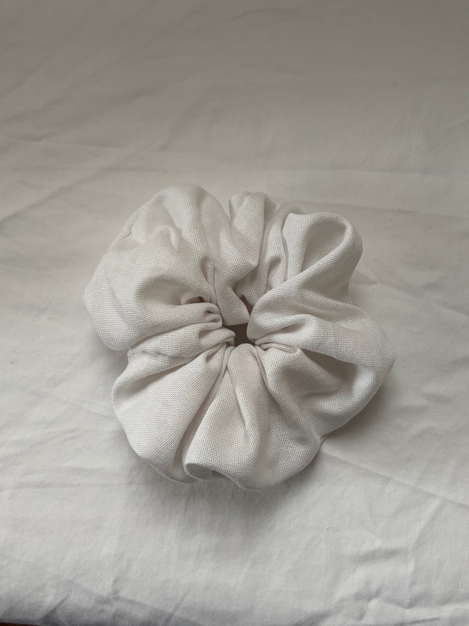 A single white fabric scrunchie made of textured linen material, photographed on white fabric background.