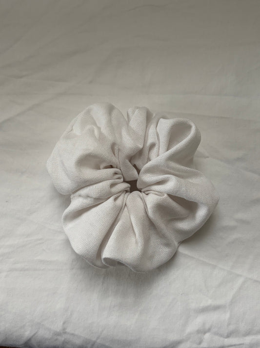 A single white fabric scrunchie made of textured linen material, photographed on white fabric background.